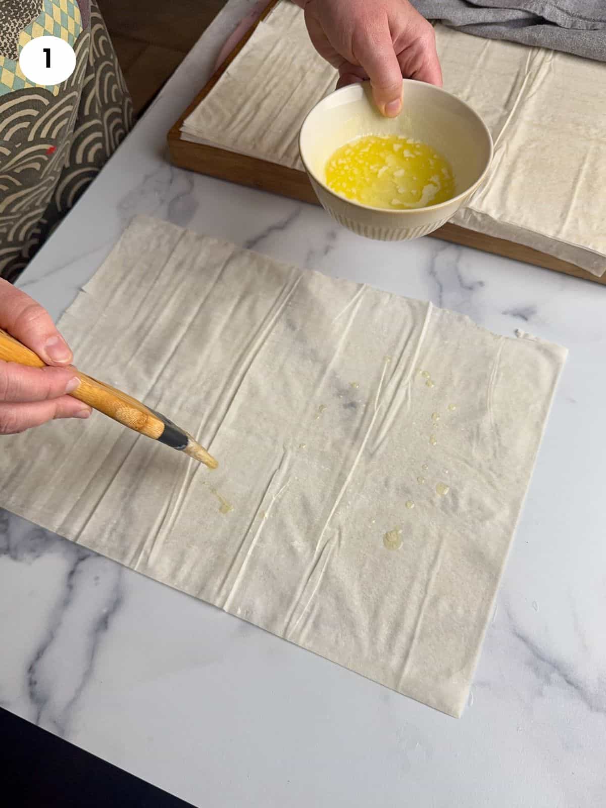 Brushing the first layer with melted butter.