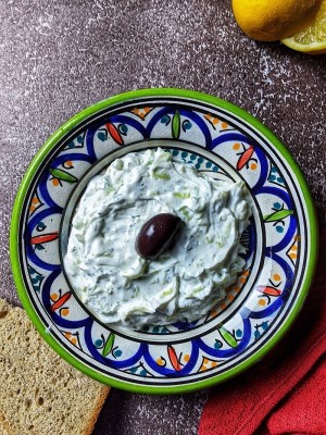 Tzatziki sauce served in bowl with olive in the middle and wholemeal bread on the side.