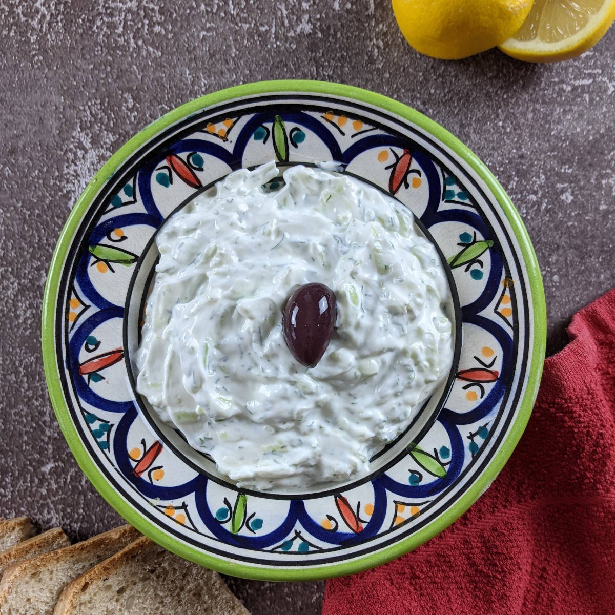 Tzatziki sauce served in bowl with olive in the middle and wholemeal bread on the side.