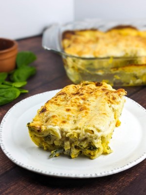 Squash and ricotta baked cannelloni served on a white plate next to tray with cannelloni.