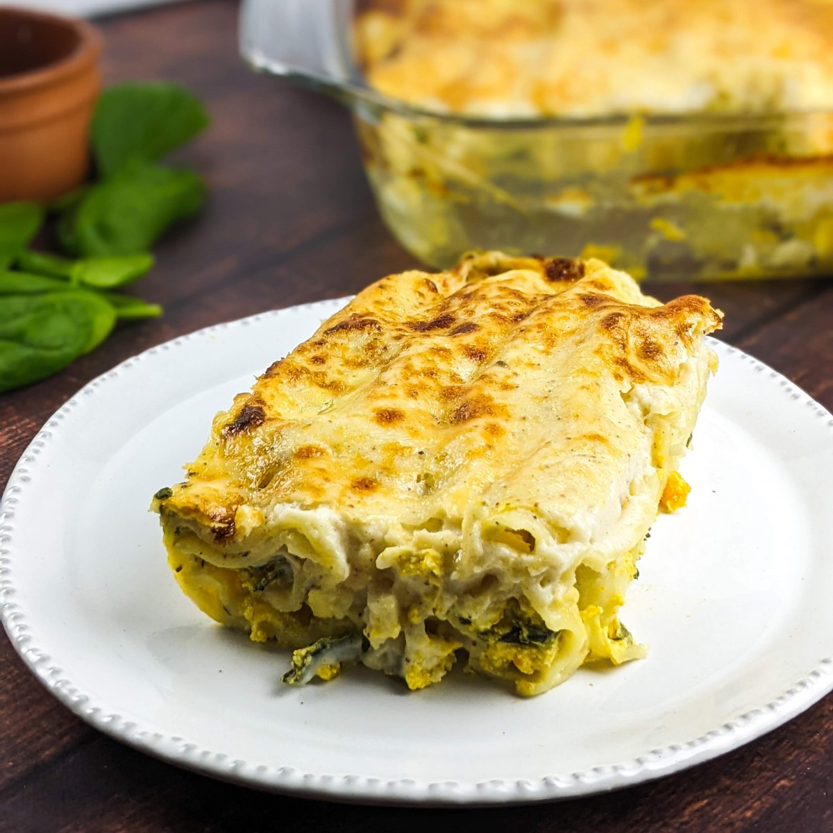 Squash and ricotta baked cannelloni served on a white plate next to tray with cannelloni.