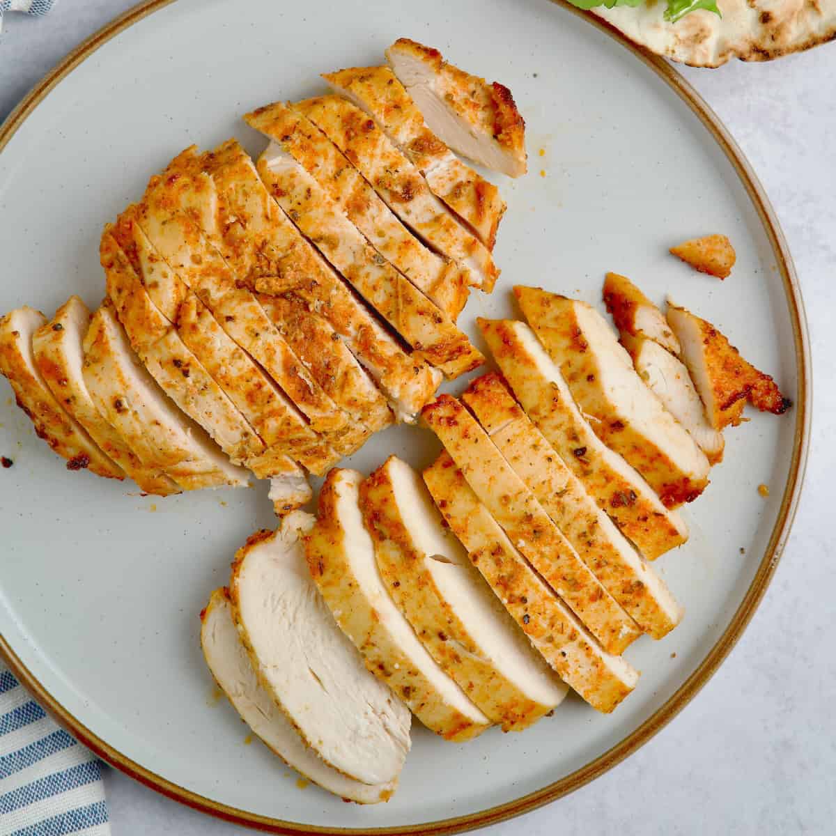 Sliced baked chicken breasts on a plate next to a wrap with a couple of chicken slices and salad.