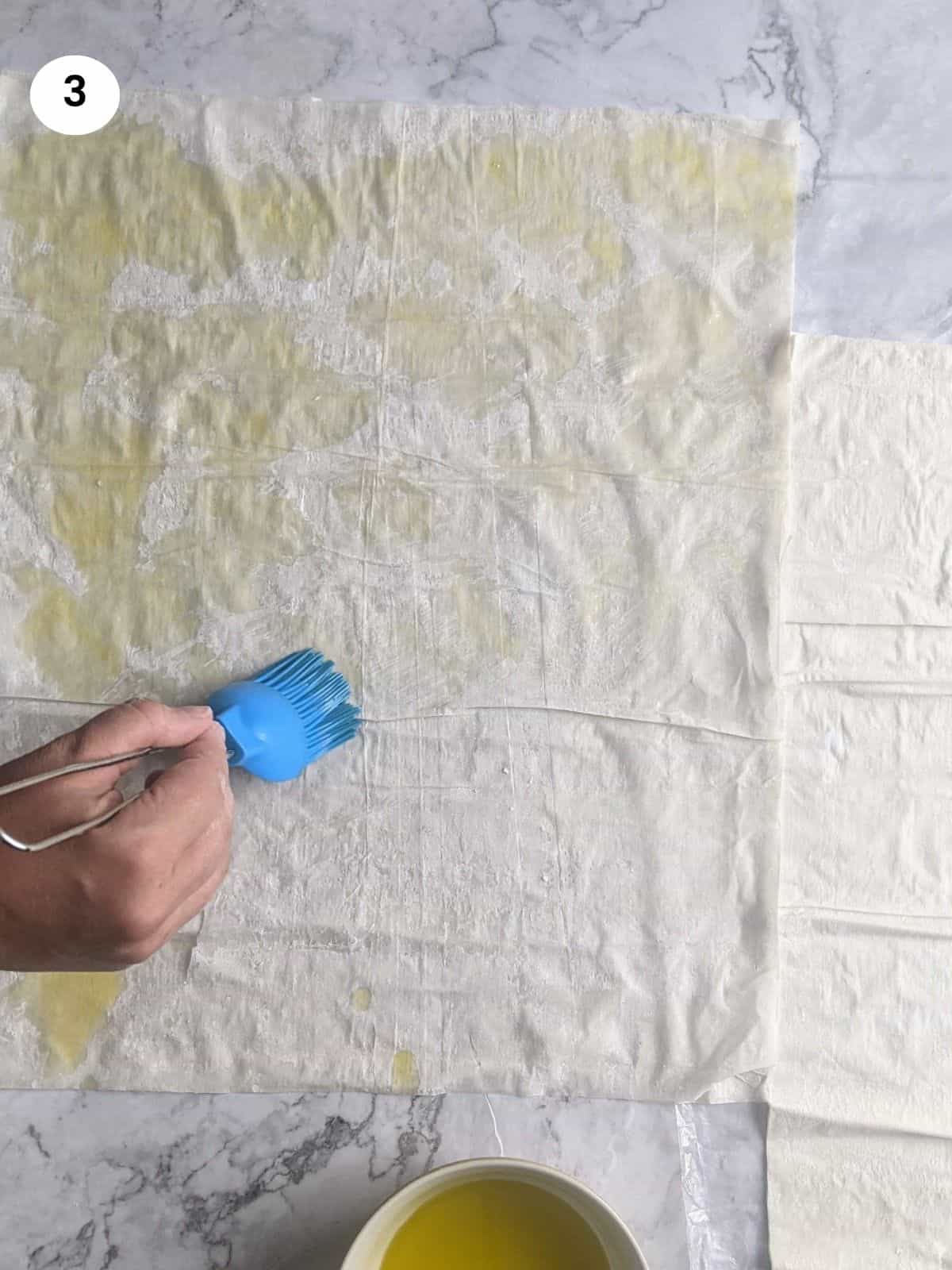 Brushing the second layer of phyllo dough with oil.