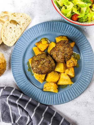 Meatballs and potatoes served on a dish next to salad and slices of bread.