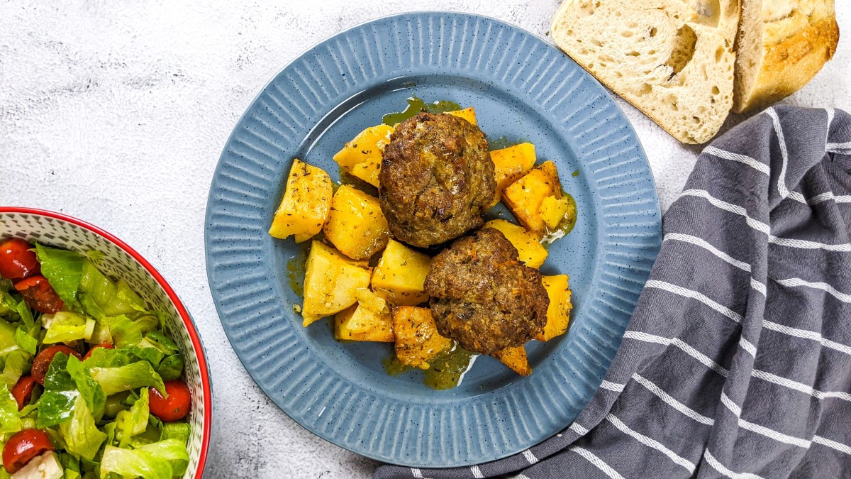 Meatballs and potatoes served on a dish next to salad and slices of bread