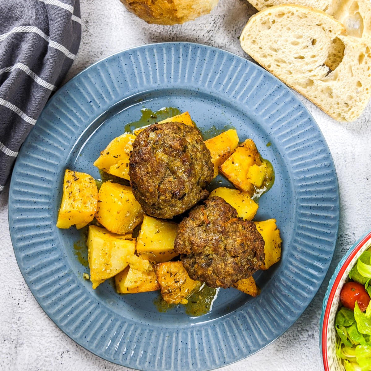 Meatballs and potatoes served on a dish next to salad and slices of bread.