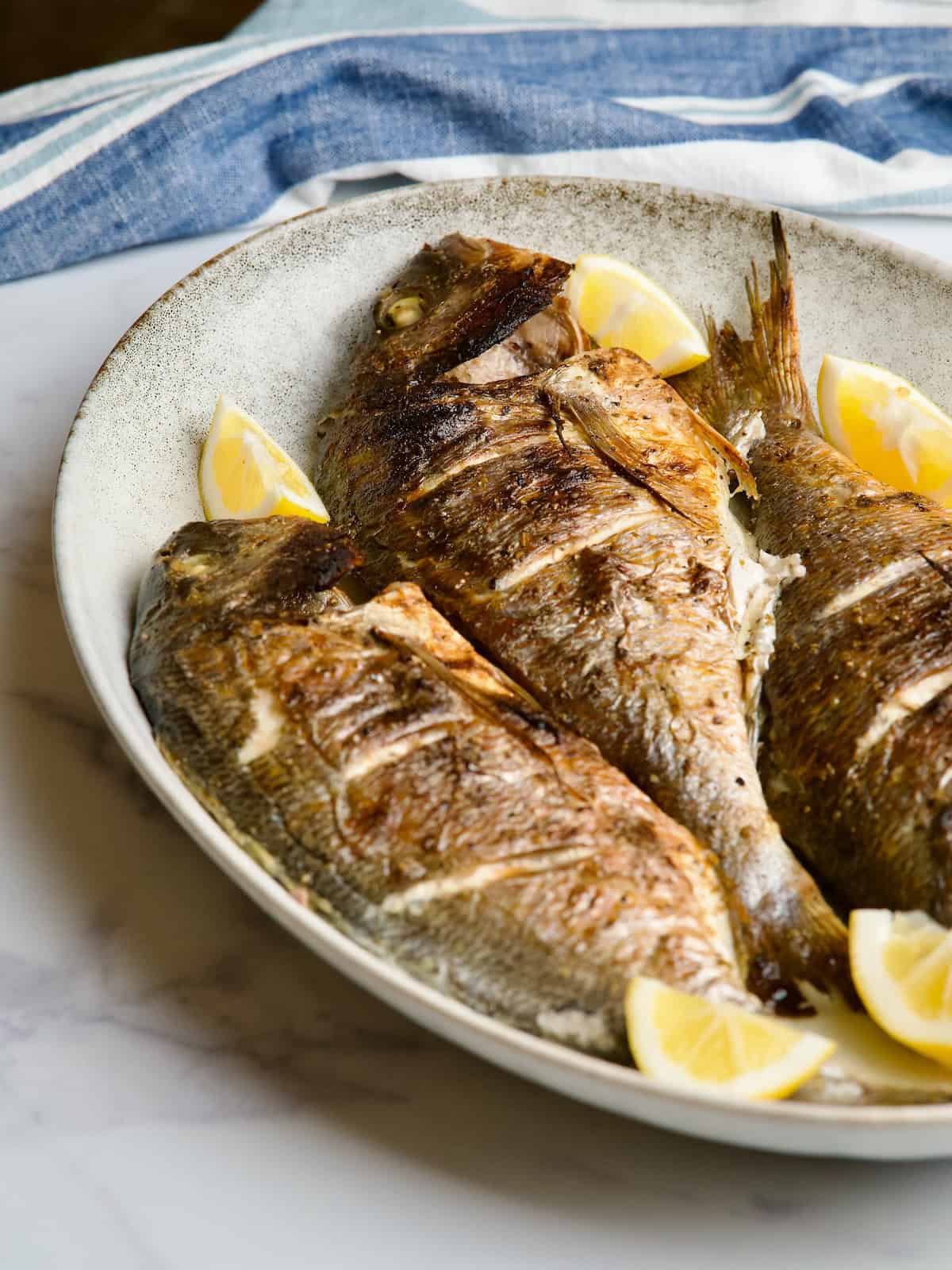 Baked sea breams served in gray platter with lemon slices Baked sea breams served in gray platter with lemon slices.
