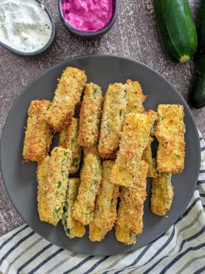 Zucchini fries on a gray plate next to bowl with yogurt dip and beetroot dip.