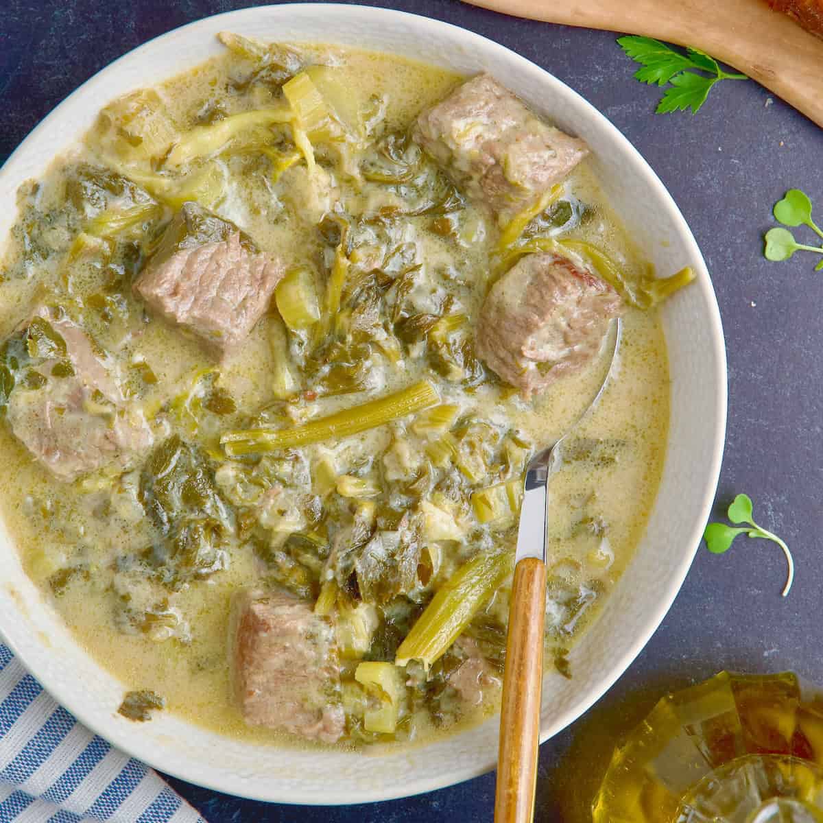 Beef and celery stew served in white bowl next to slices of bread and lemon slices.