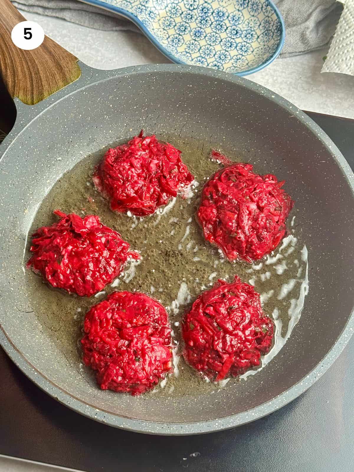 Beet fritters in a pan cooking on one side.