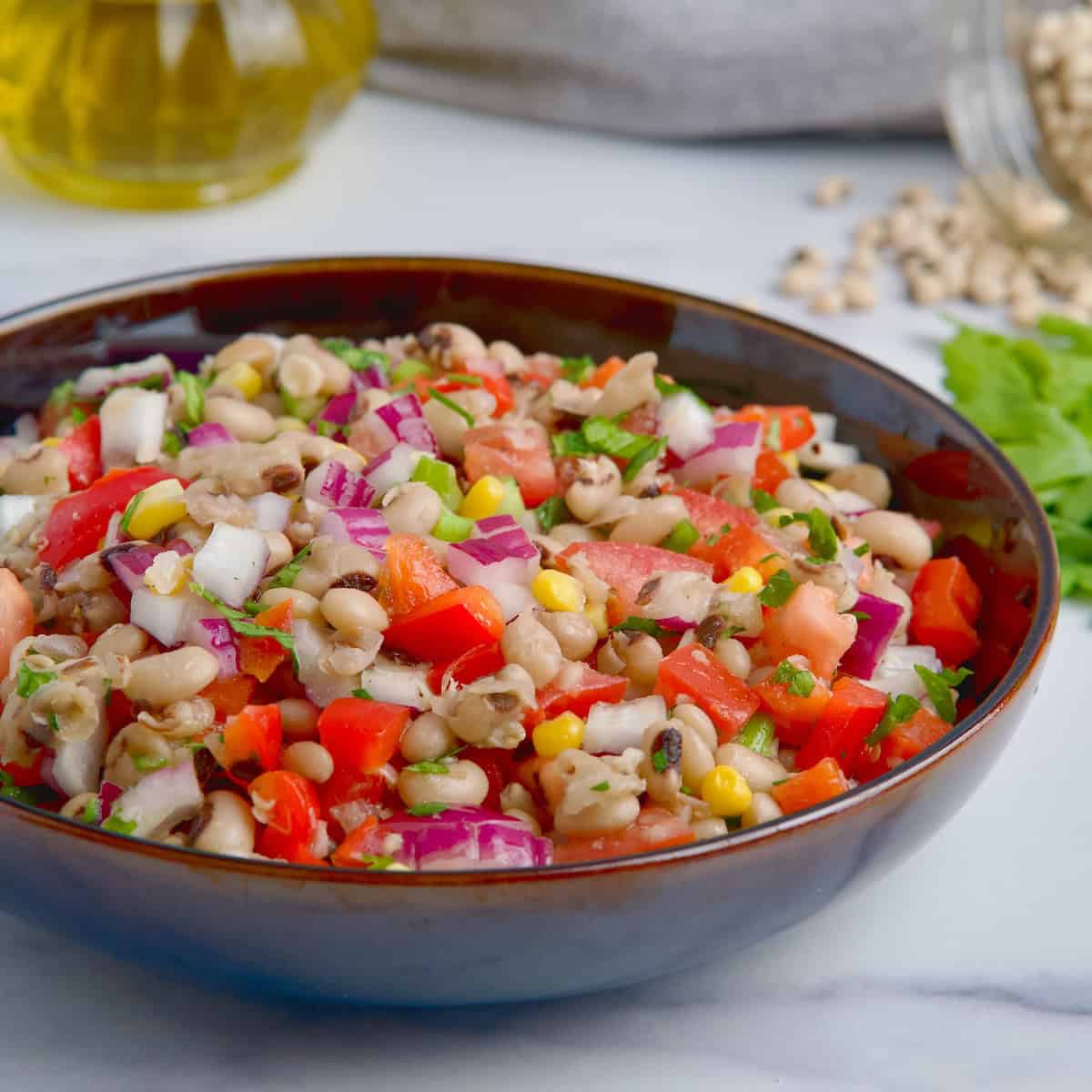 Black eyed peas and veggie salad on a black bowl next to olive oil and fresh parsley.