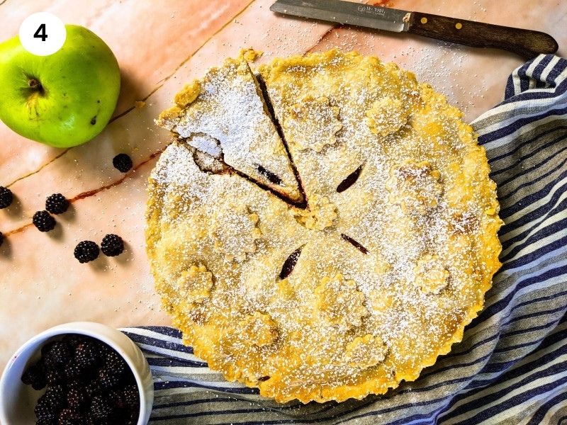 Apple blackberry pie on a serving plate with one slice cut.