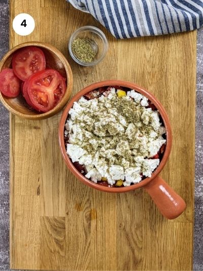 Adding feta cheese and oregano to the ovenproof dish.