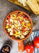 Baked feta cheese with tomatoes in an ovenproof dish next to bread, olives and tomatoes.
