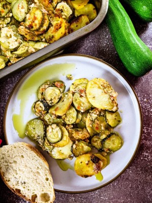 Greek zucchini and potato casserole served on a plate with a slice of bread next to baking tray.