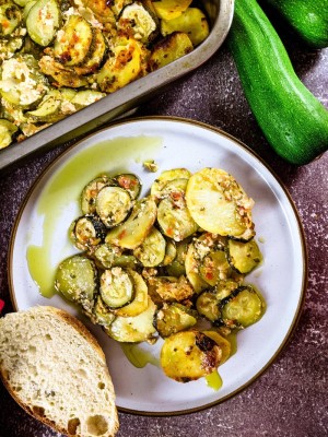 Greek zucchini and potato casserole served on a plate with a slice of bread next to baking tray. Greek zucchini and potato casserole served on a plate with a slice of bread next to baking tray.