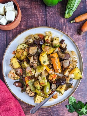 Briami casserole served on a plate next to raw vegetables and a bunch of parsley.