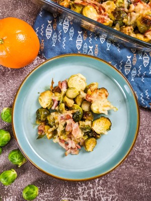 Roasted brussels sprouts with bacon and parmesan served on blue plate next to raw brussels sprouts and orange.
