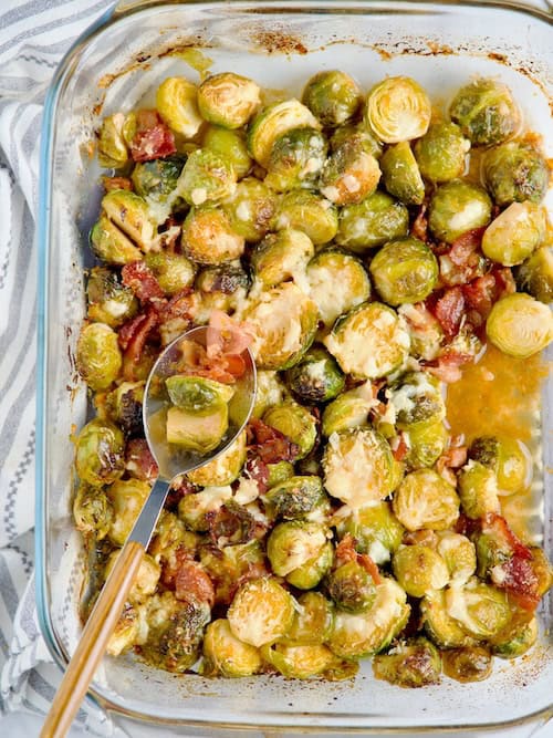 Roasted brussels sprouts with bacon and parmesan served on blue plate next to raw brussels sprouts and orange.