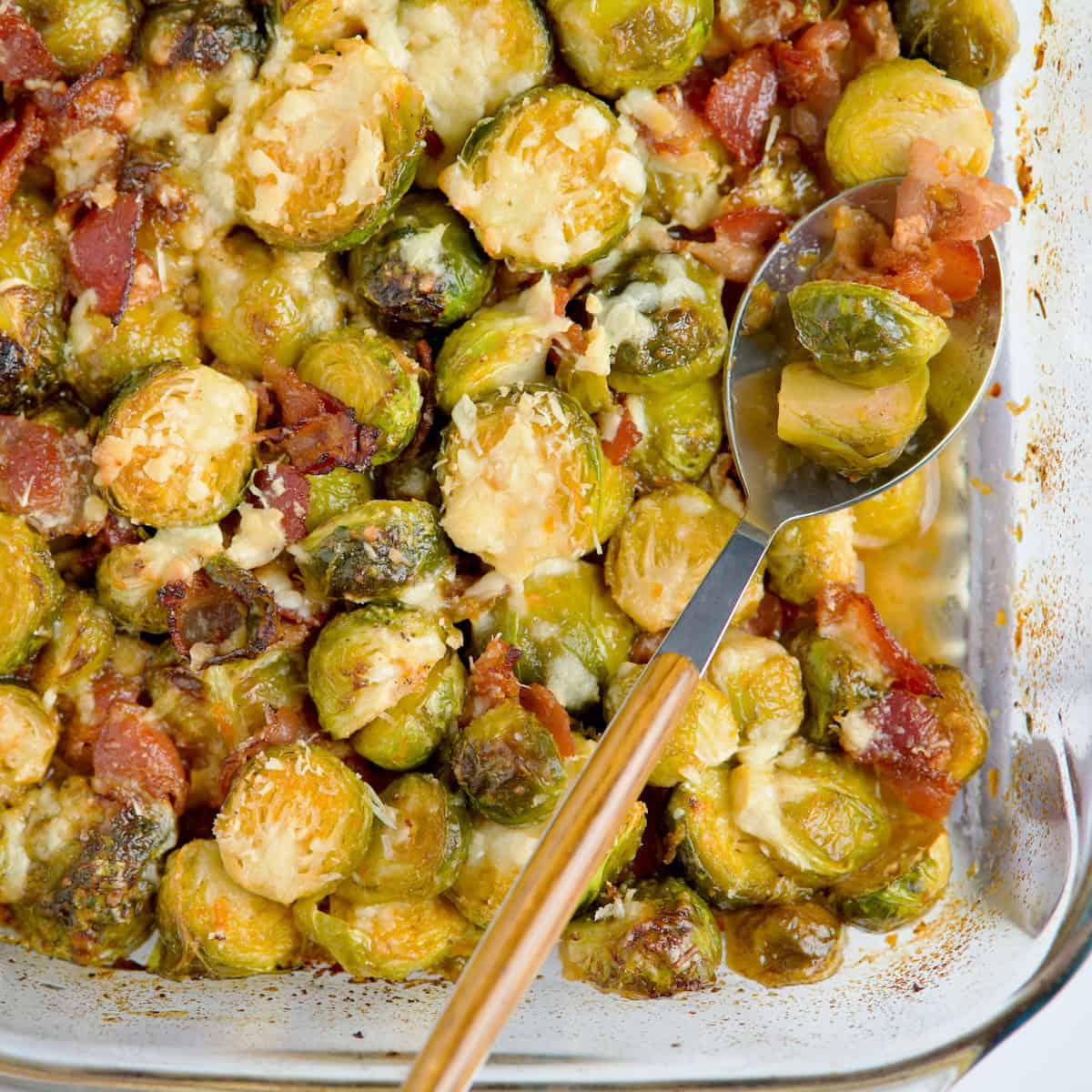 Roasted brussels sprouts with bacon and parmesan served on blue plate next to raw brussels sprouts and orange.