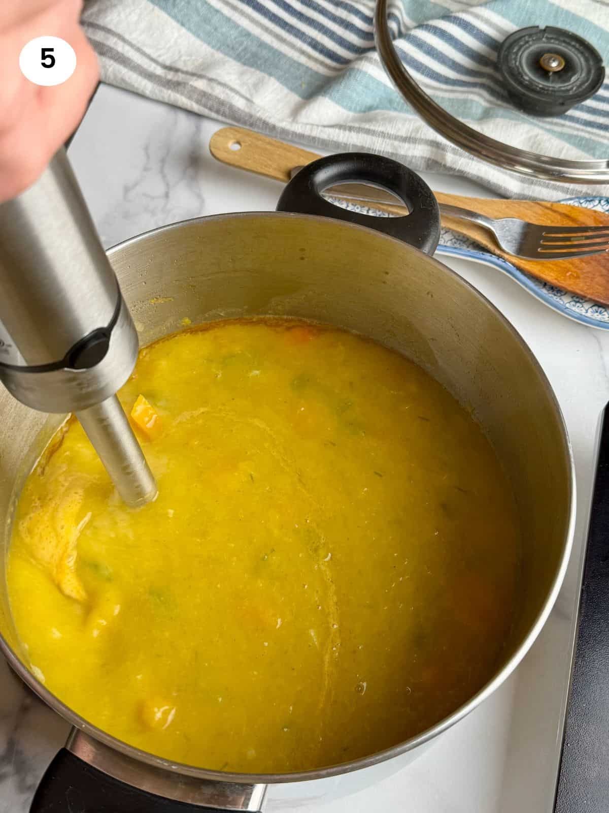 Blending the soup with an immersion blender.