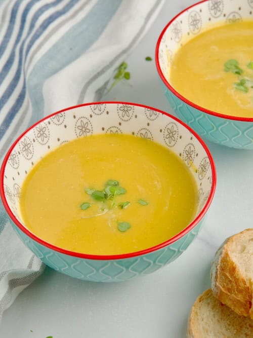 Butternut squash and leeks soup served in bowl next to slices of bread.