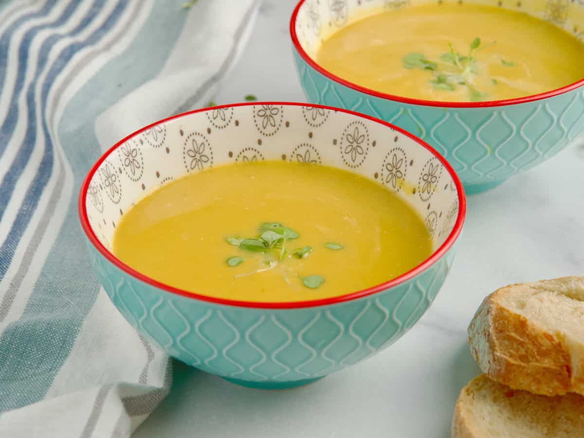 Butternut squash and leeks soup served in blue bowls next to slices of bread.