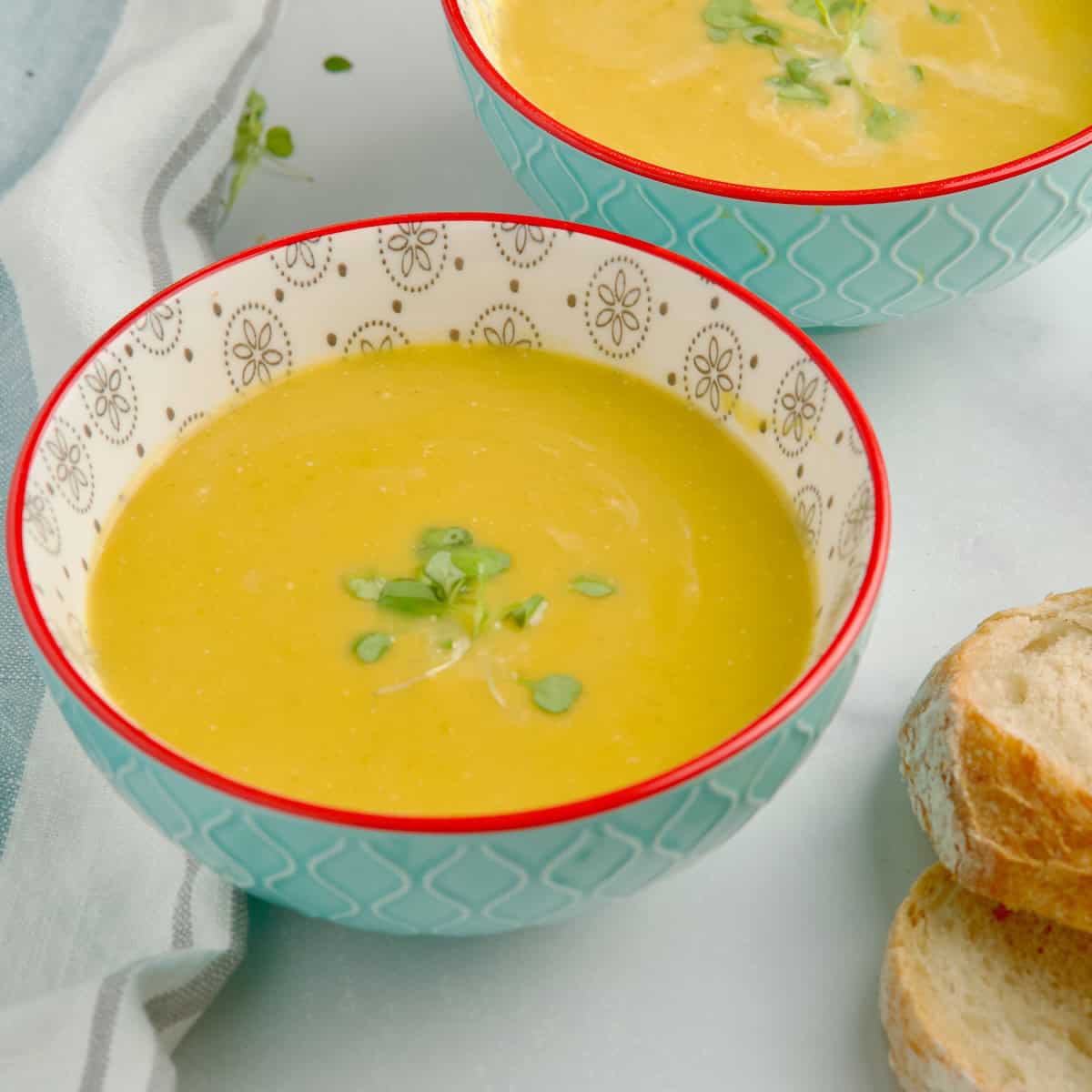 Butternut squash and leeks soup served in bowl next to slices of bread.