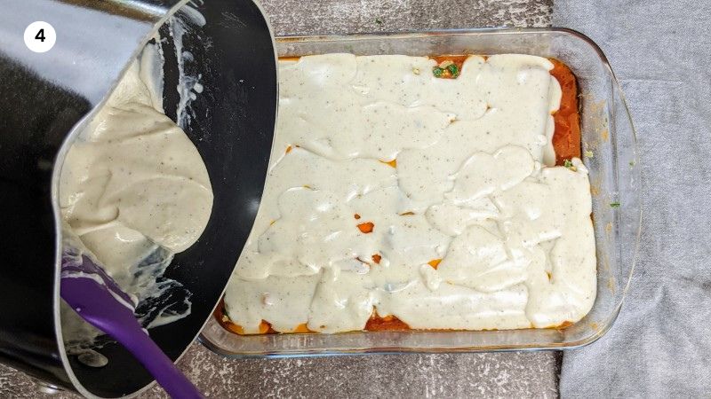 Adding the white sauce on top of the cannelloni.