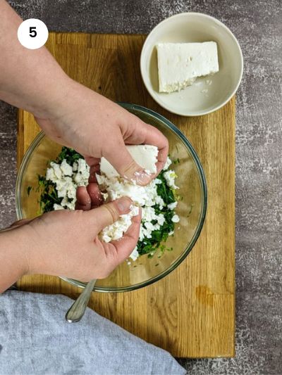 Adding the crumbled feta cheese to the spinach for the cannelloni filling.