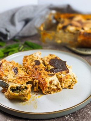 Spinach and feta cannelloni served on a white plate next to tray with cannelloni.