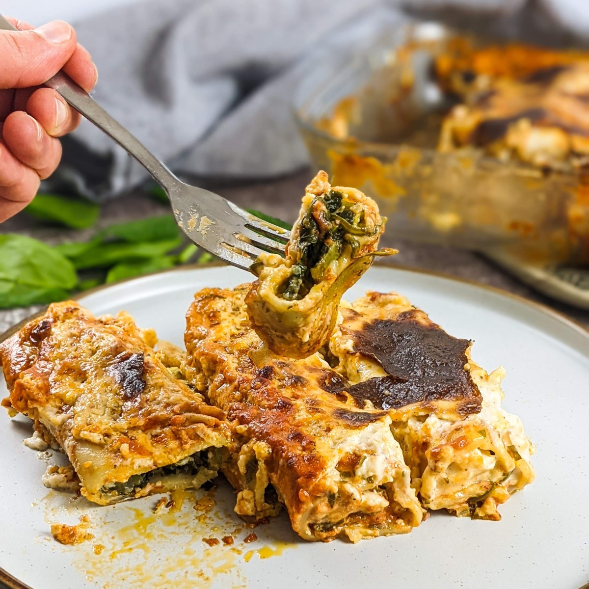 Spinach and feta cannelloni served on a white plate next to tray with cannelloni.