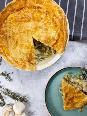 Celery, mushroom and chicken pie slice with the whole pie dish next to it and some thyme and mushrooms.