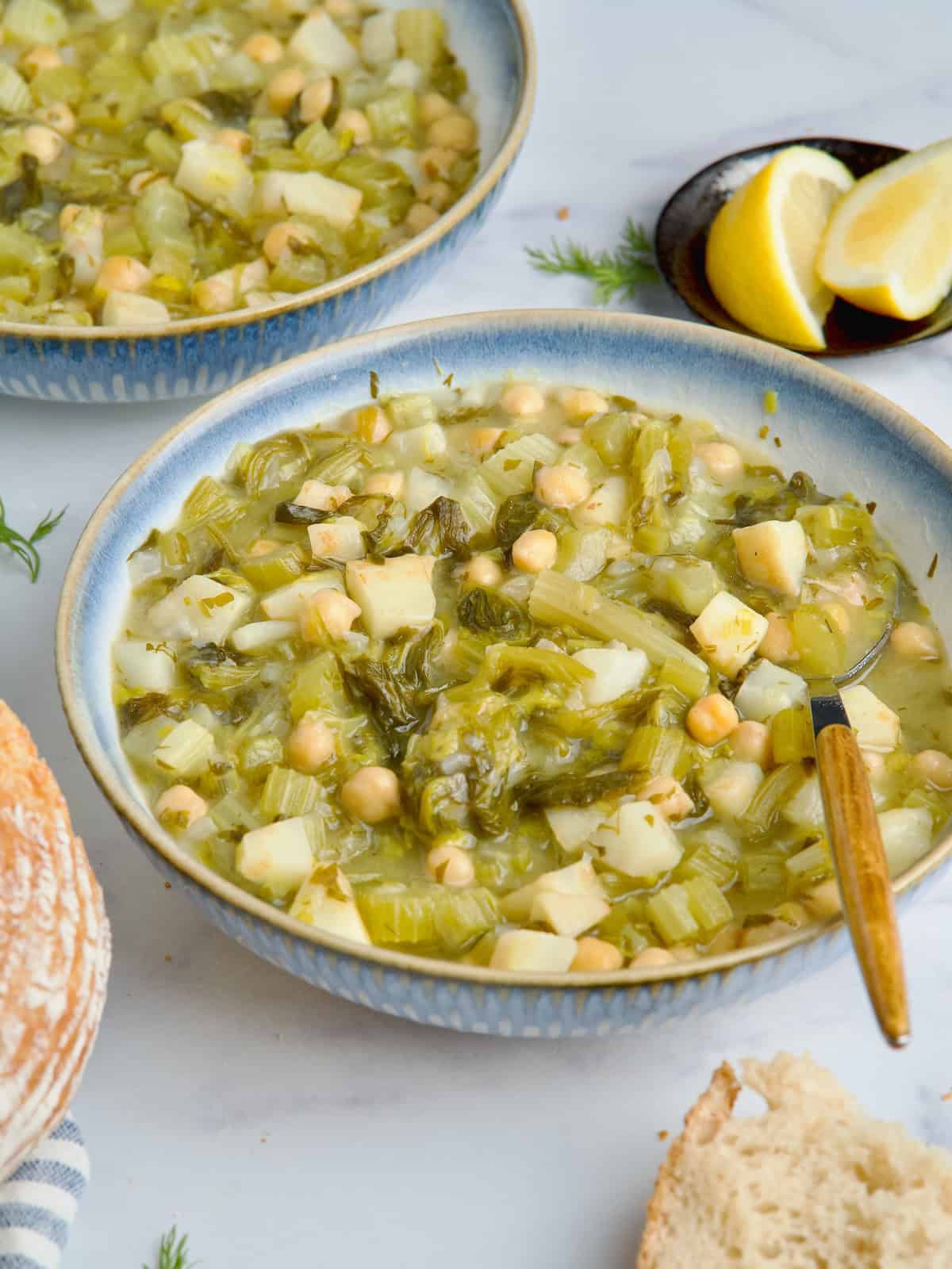 Chickpea and celery stew served in a white bowl with slices of bread on the side.