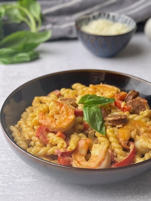 Chorizo and shrimp pasta served in black bowl with some basil on top.