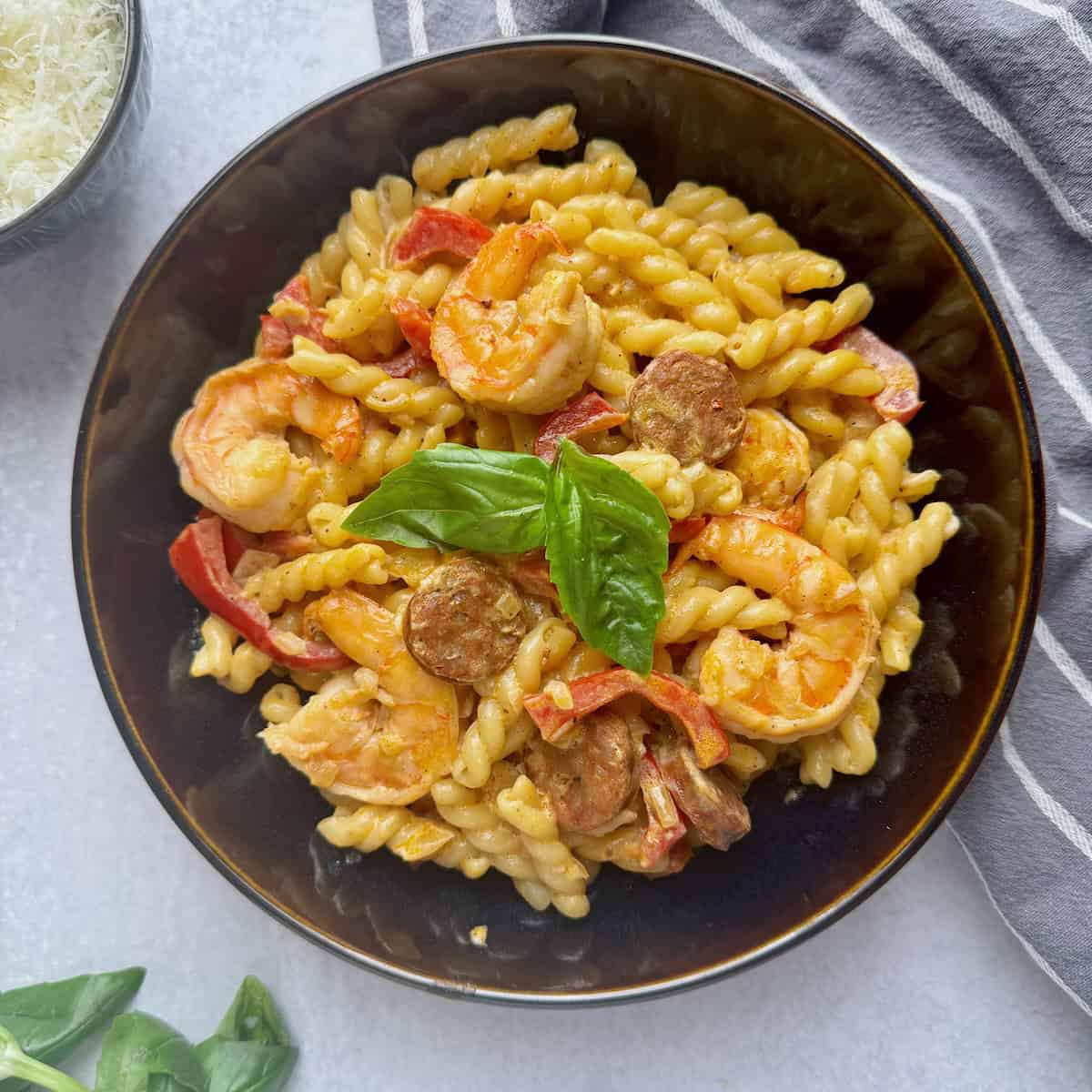 Chorizo and shrimp pasta served in black bowl with some basil on top.