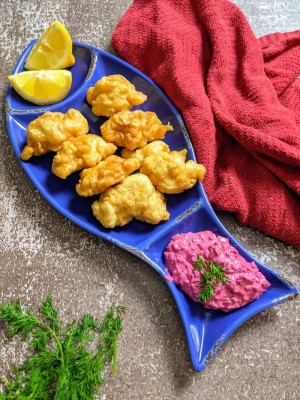 Cod fillet bites served on a fish plate with two slices of lemon and beetroot & yogurt dip