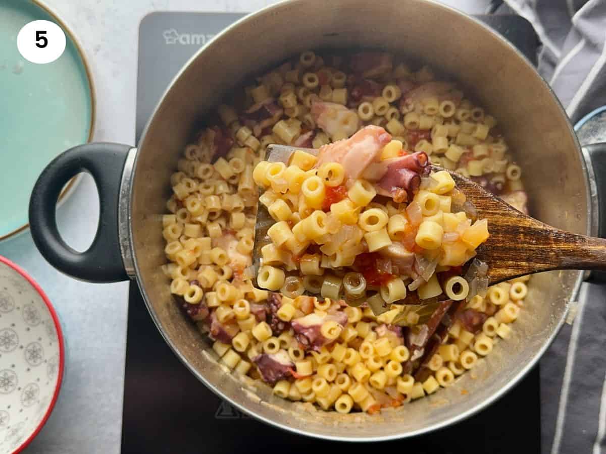 Cooked octopus with pasta on wooden spatula.