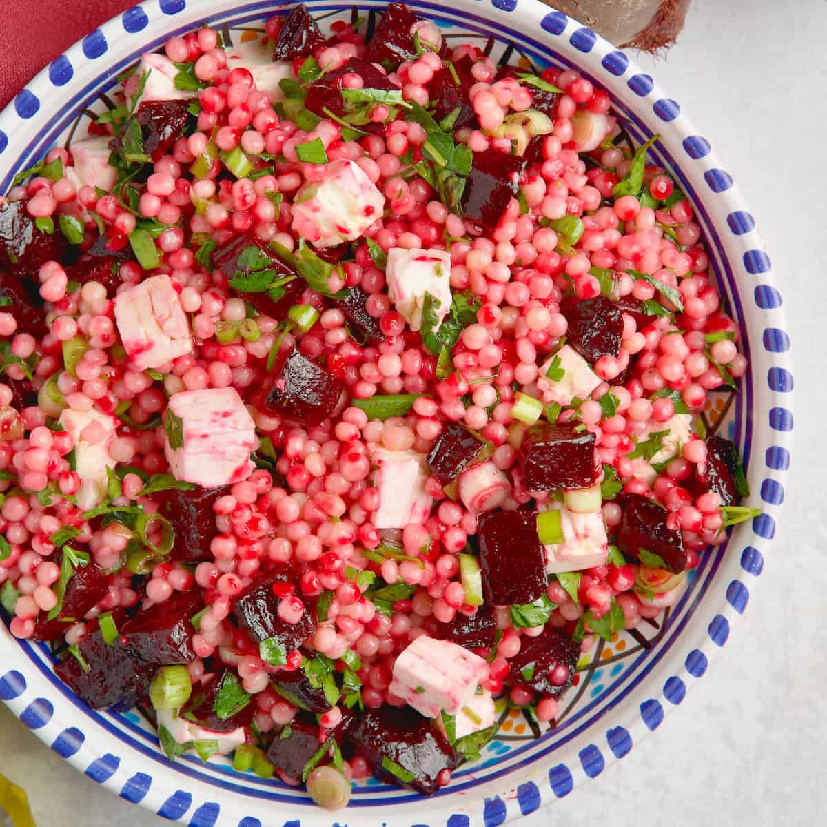 Couscous salad with roasted beets and feta on a bowl next to olive oil and beets.