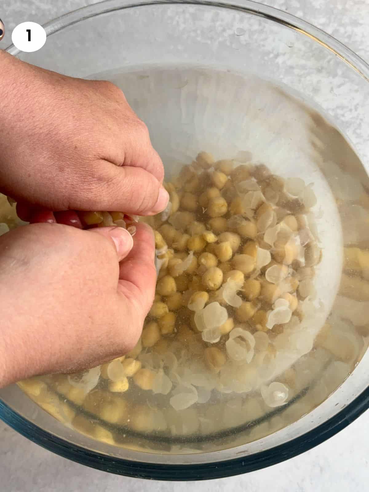 Peeling chickpeas soaked in a bowl of water.