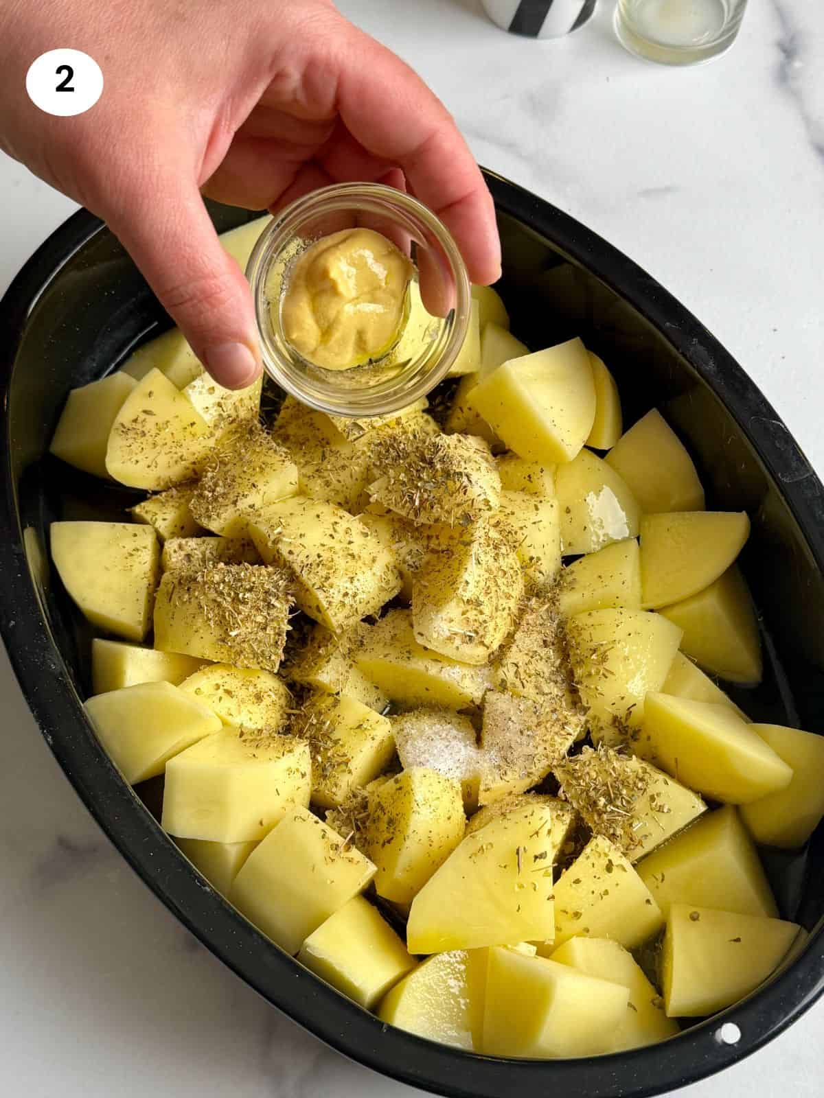 Adding mustard to the tray with the potatoes.