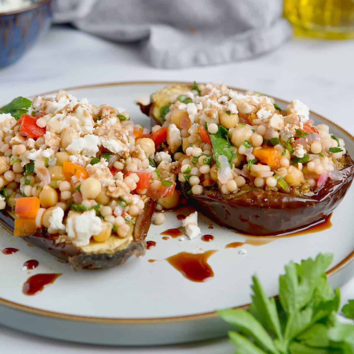 Roasted eggplants with couscous filling served on a white plate with feta cheese and balsamic glaze.