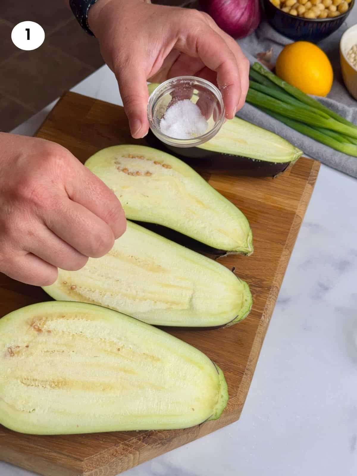 Sprinkling salt on half eggplants.