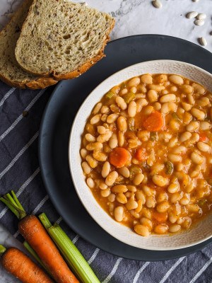Greek white bean soup served on a bowl next to bread and vegetables.