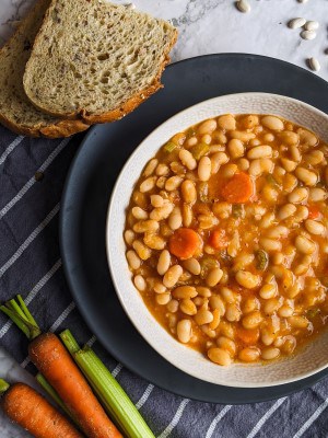 Greek white bean soup served on a bowl next to bread and vegetables. Greek white bean soup served on a bowl next to bread and vegetables.