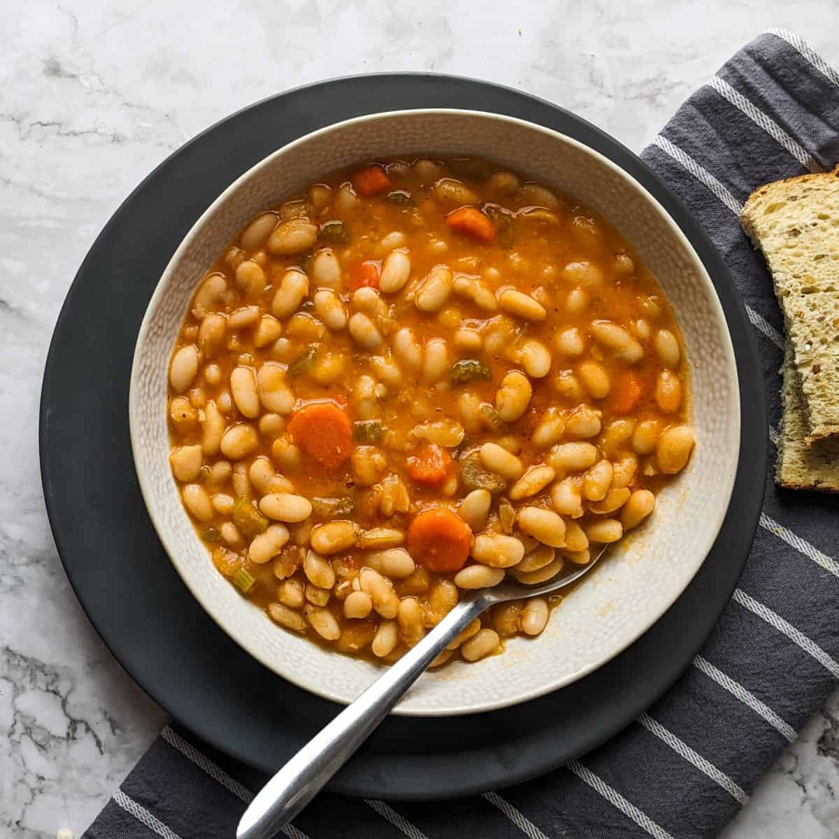 Greek white bean soup served on a bowl next to bread and vegetables.