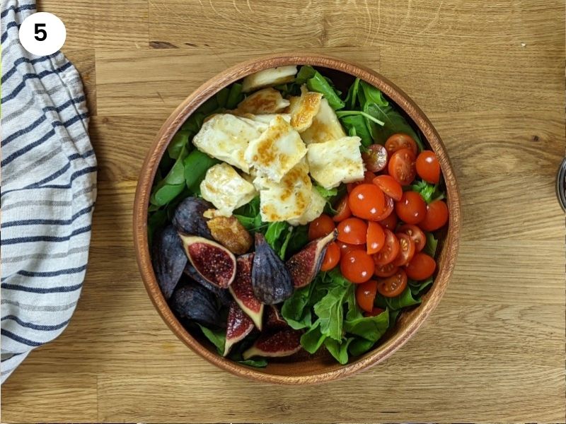 Fig and grilled halloumi salad in wooden bowl before adding dressing.