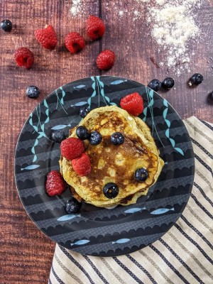 Pancakes το ένα πάνω στο άλλο με μούρα και σιρόπι σφενδάμου να τρέχει από πάνω.