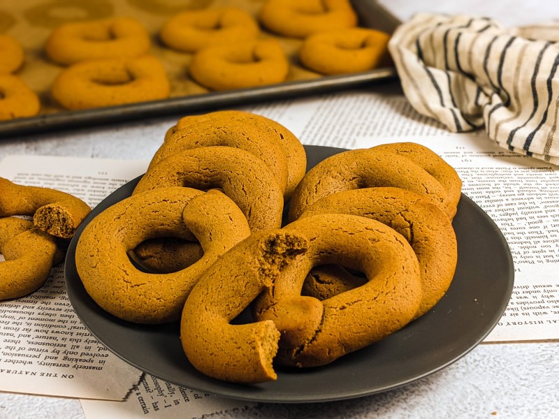 Grape molasses cookies served on a gray plate next to tray with cookies.