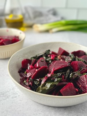 Greek beet salad served on a white bowl with green onions and olive oil bottle in the background.